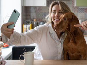 woman pointing phone at vizsla dog