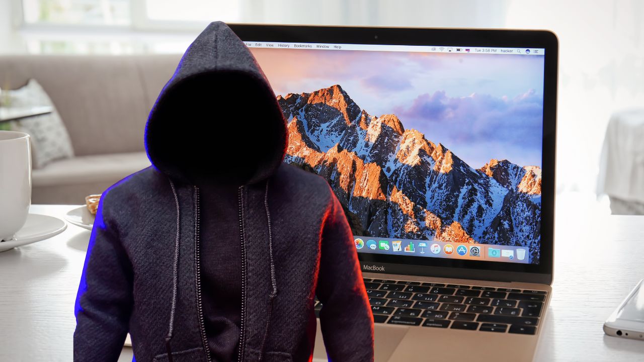 person in hoodie with macbook behind them