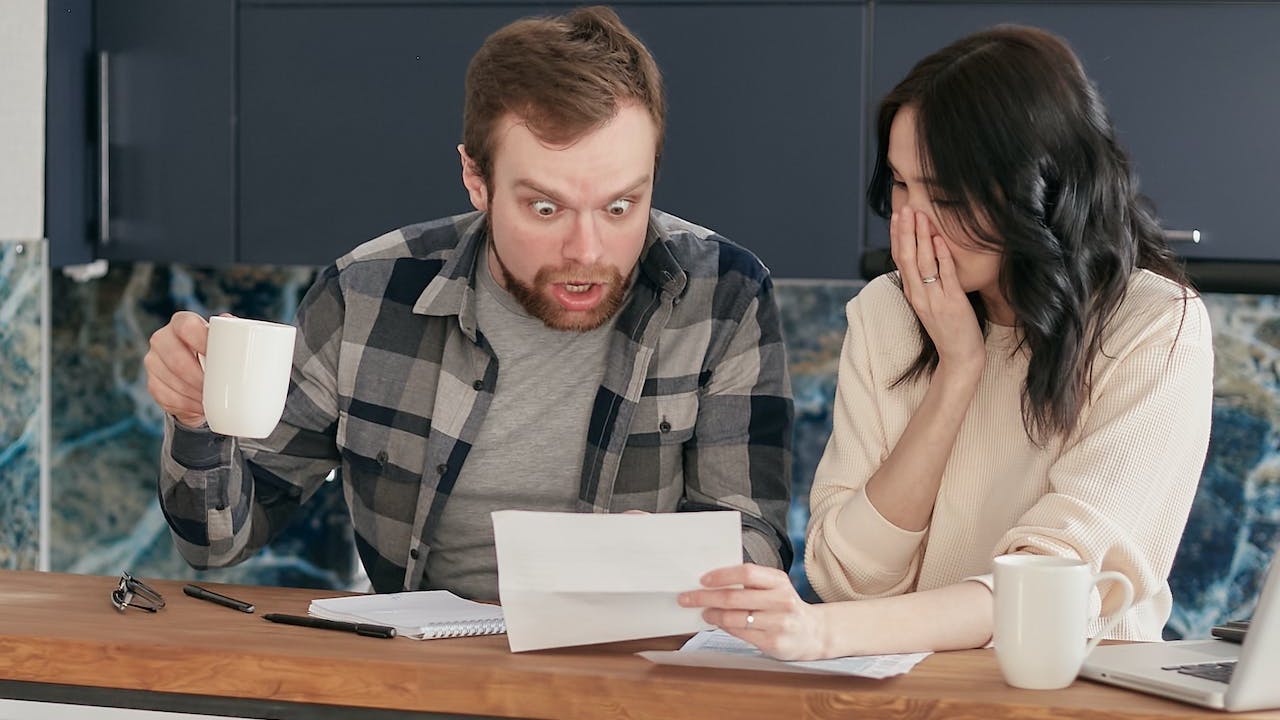 a couple sitting near the wooden table while looking at the document in shocked emotion