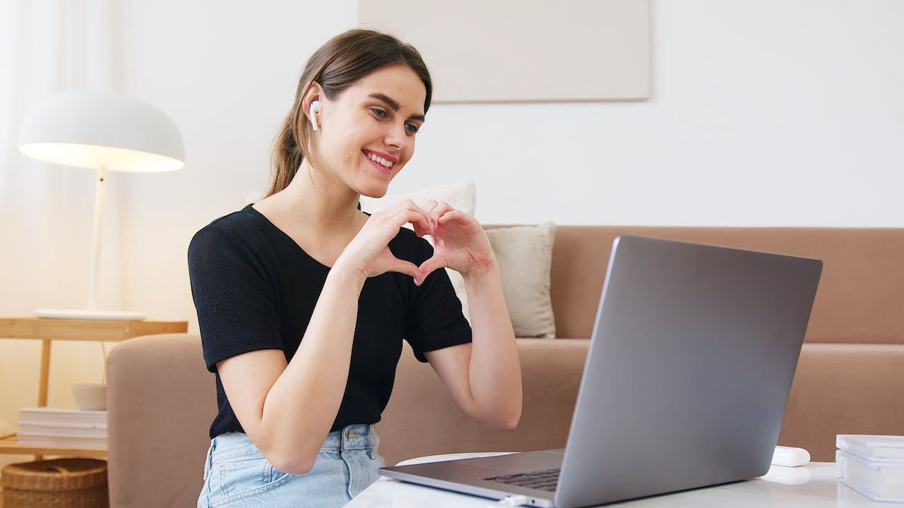 Woman in front of laptop making a heart symbol with hands