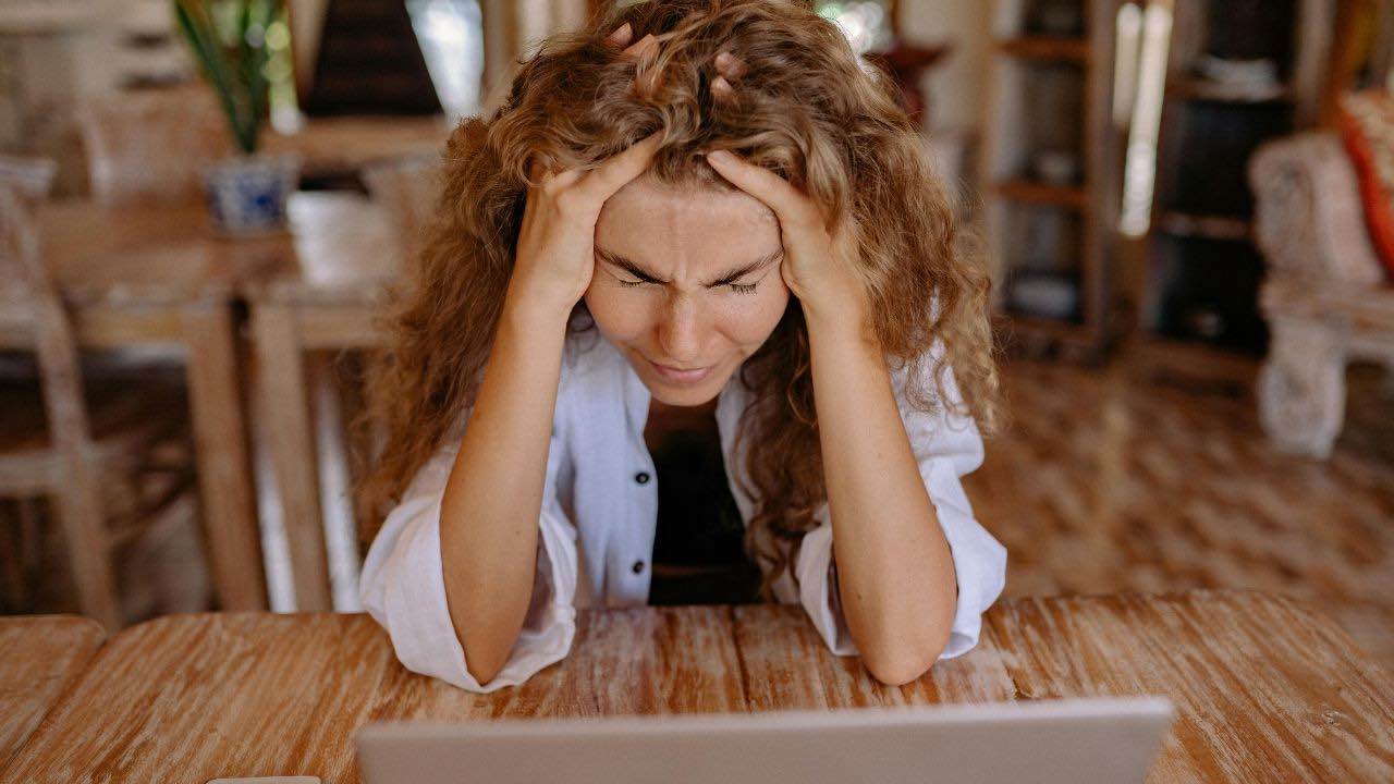 a person sitting at a table with their head in their hands while looking at their laptop frustrated