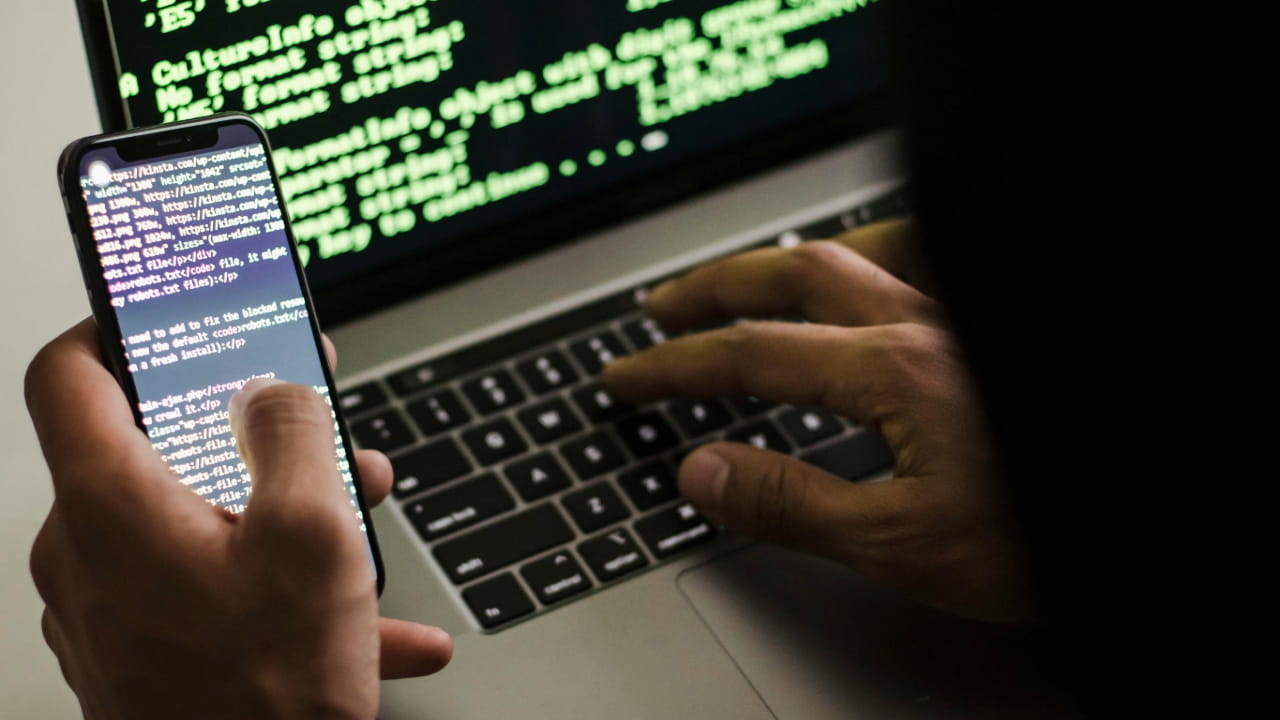 A person using computer, holding a smartphone in one hand.