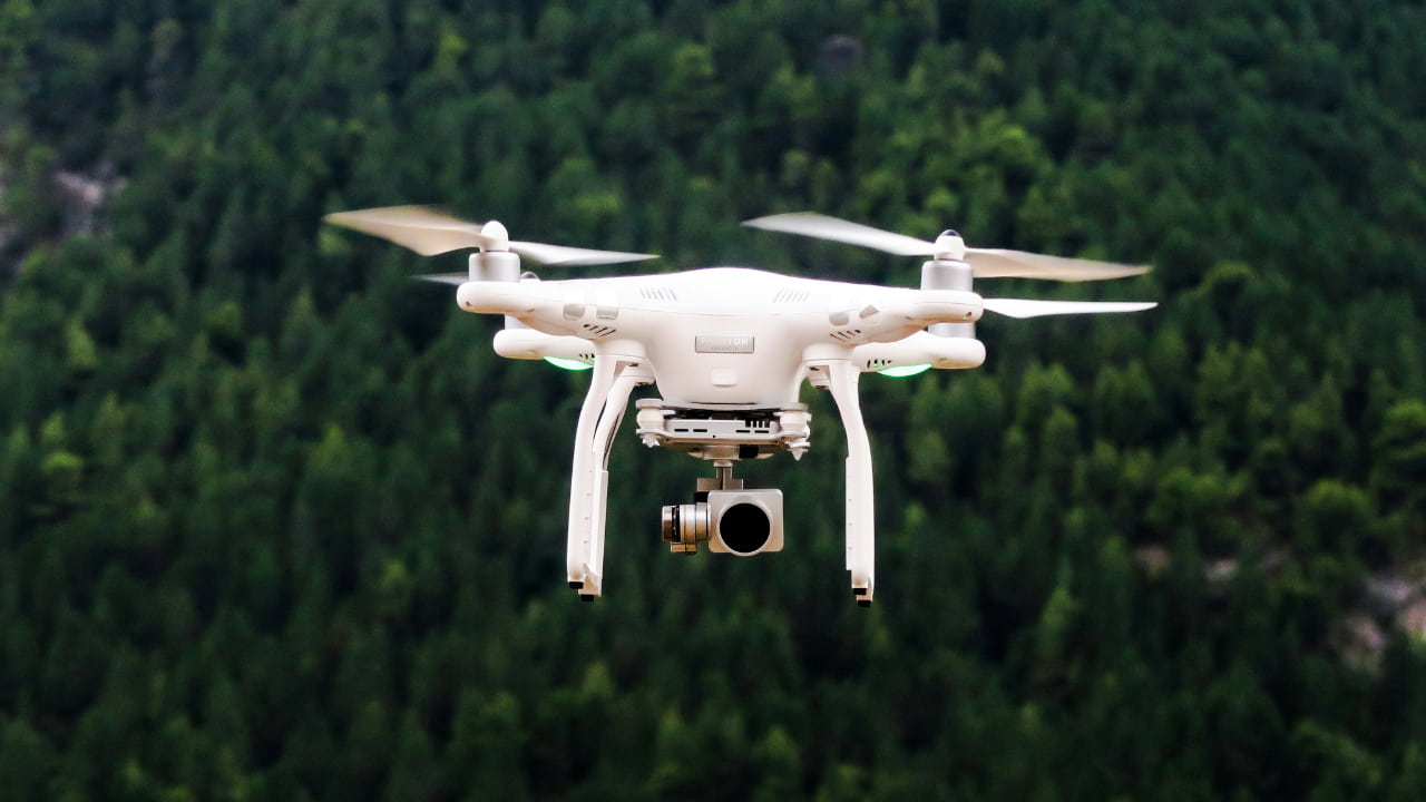 A drone flying with greenery in the background.