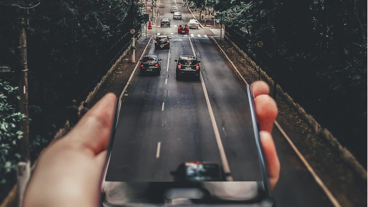 Forced Perspective Photography of Cars Running on Road Below Smartphone