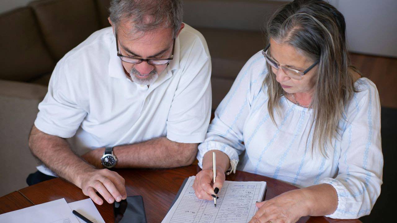 Elderly Couple Sitting at the Table with Documents and Using a Smartphone