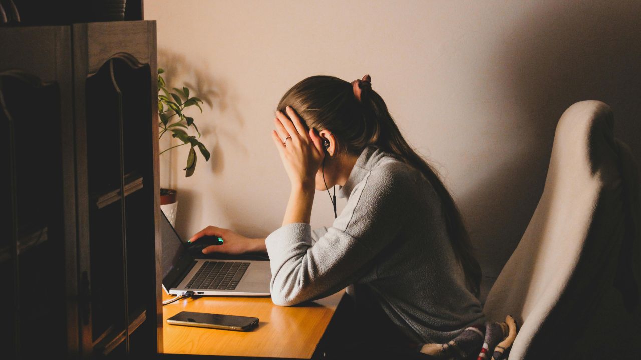 A woman sitting in front of a computer with her hands on her head.