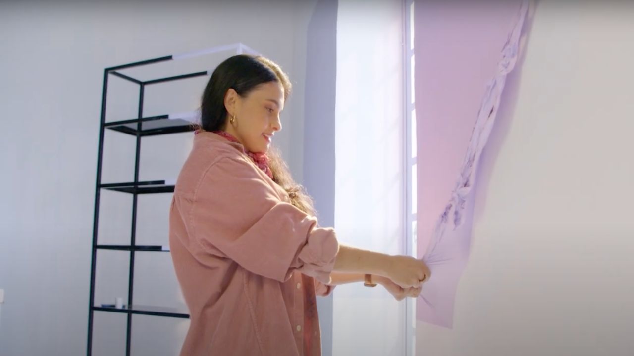 A woman peeling off peelable paint from the wall 