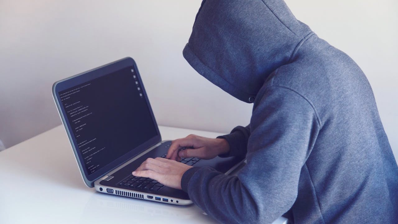 Anonymous hacker with on laptop in white room