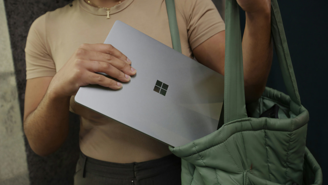 A person putting a Microsoft laptop in a bag.