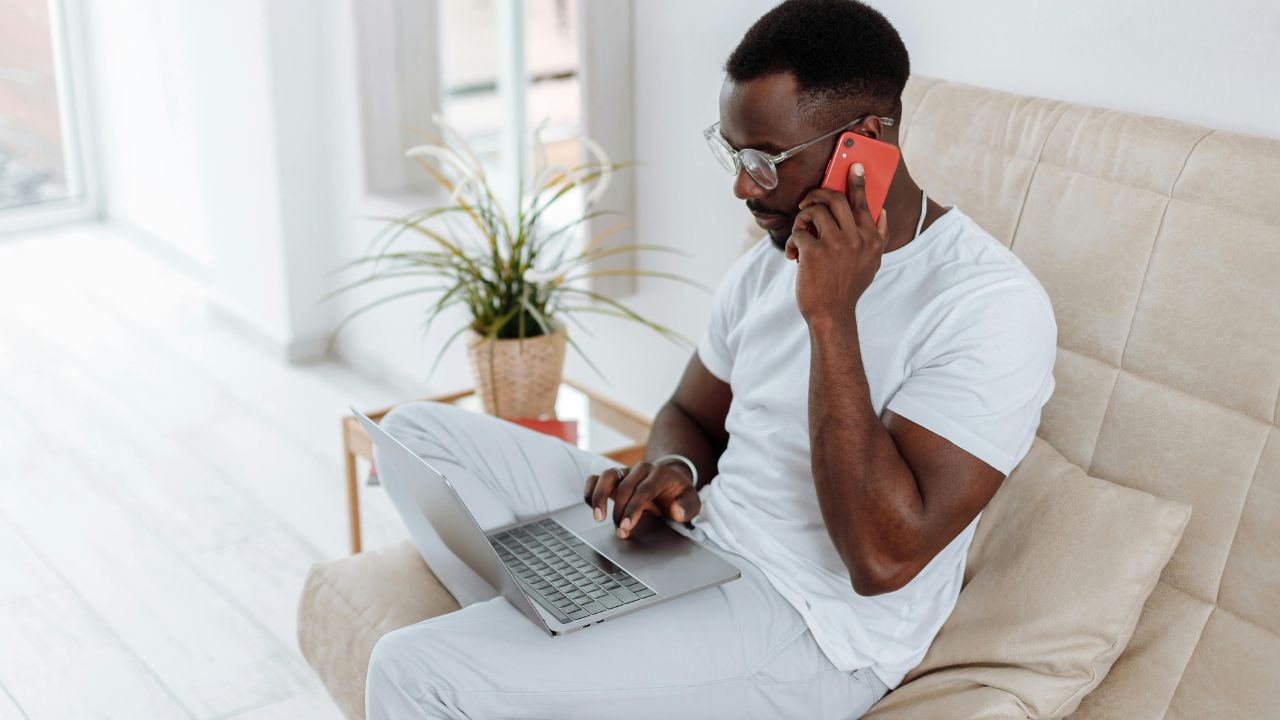 A man speaking on his cell phone and typing on his laptop 