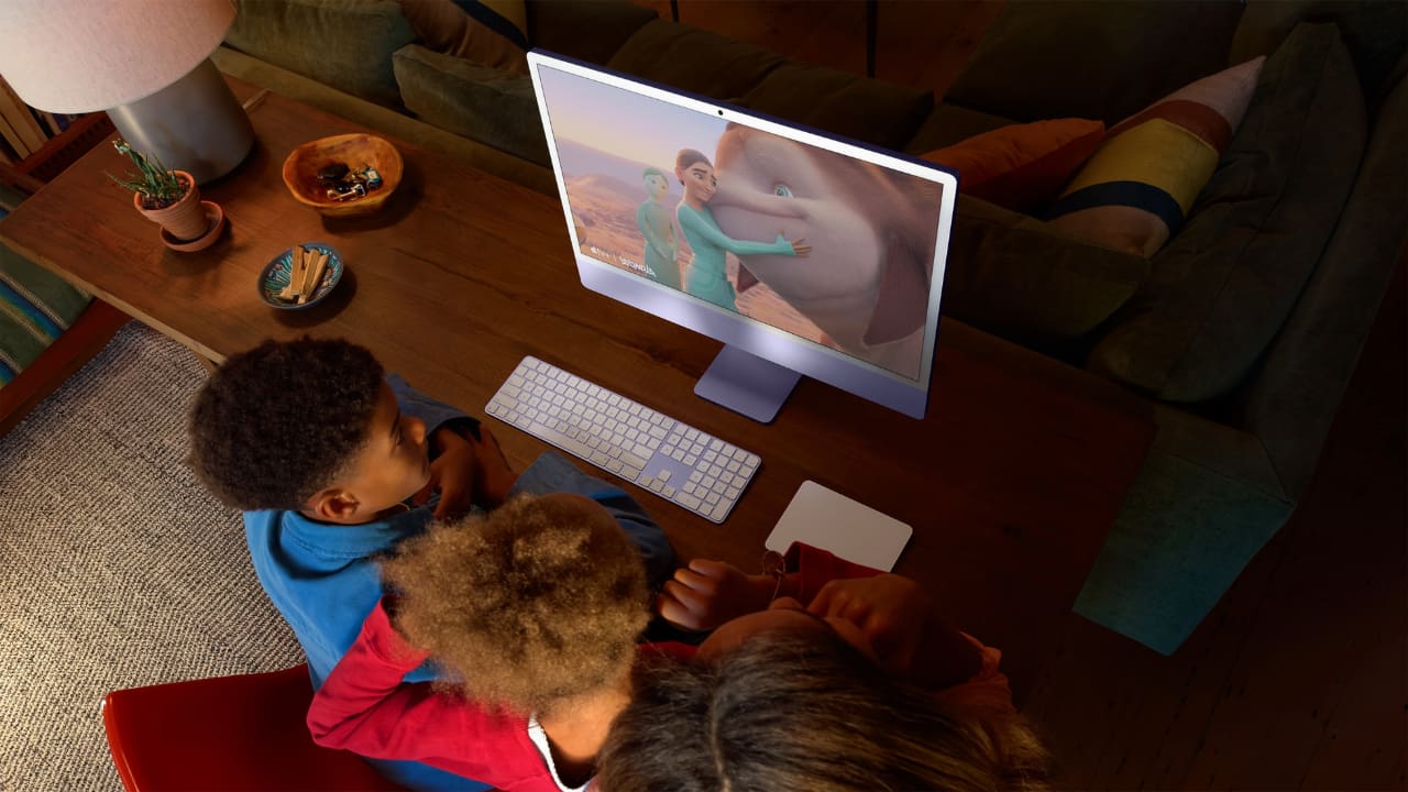 Apple Mac on a table with kids sitting in front of it