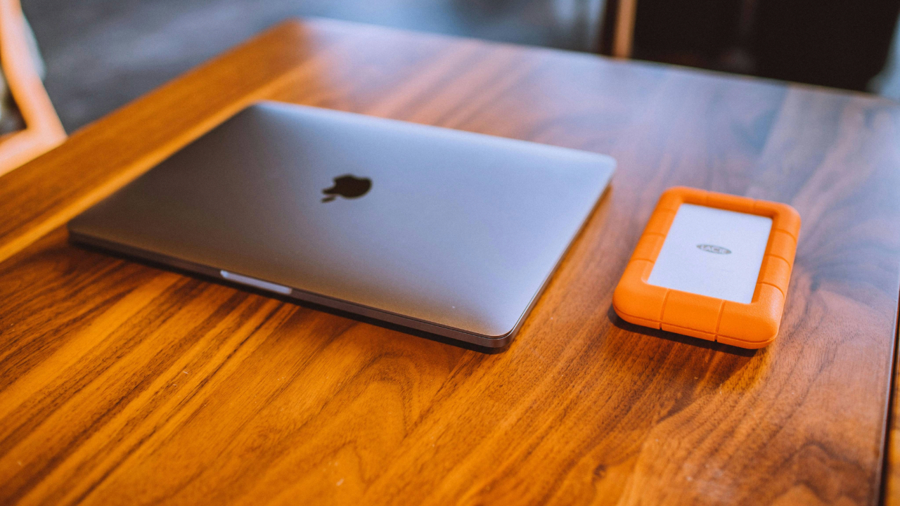 A stock photo showing an Apple MacBook next to a LaCie external hard drive.