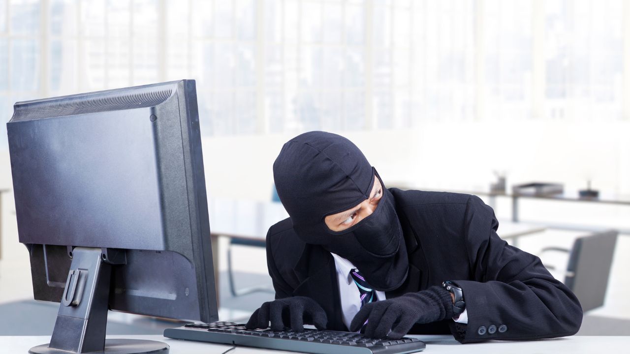 A person wearing mask and sneaking on a computer.