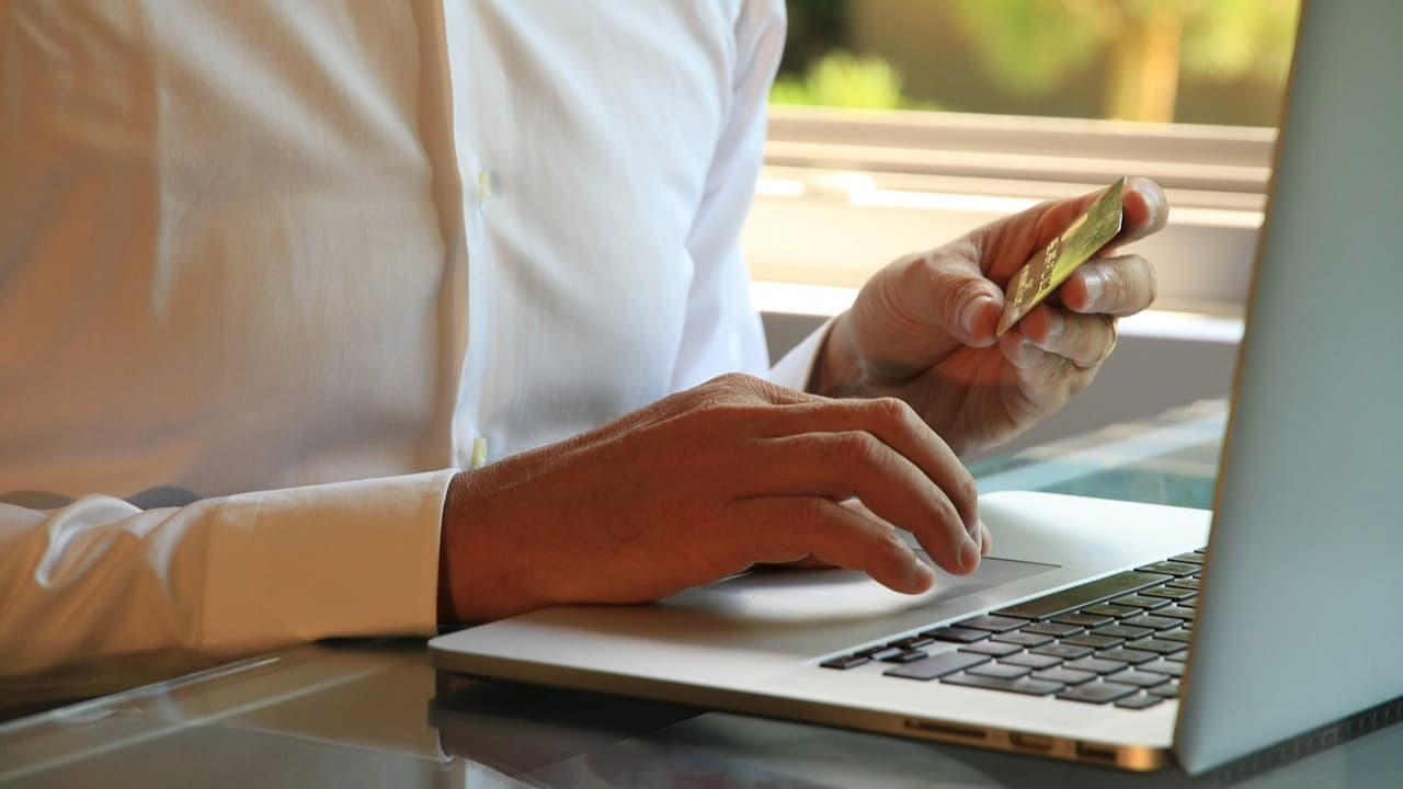 A person using laptop with a card in one hand