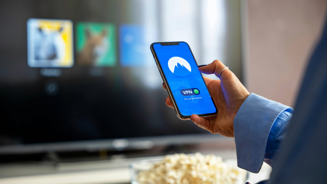 A stock photo showing a smartphone using a VPN and Netflix on a TV in the background.