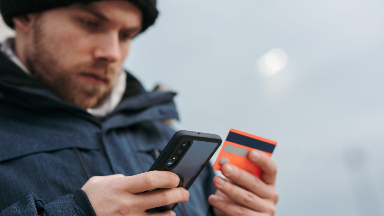 Man looking at his credit card in one hand and his phone in the other 