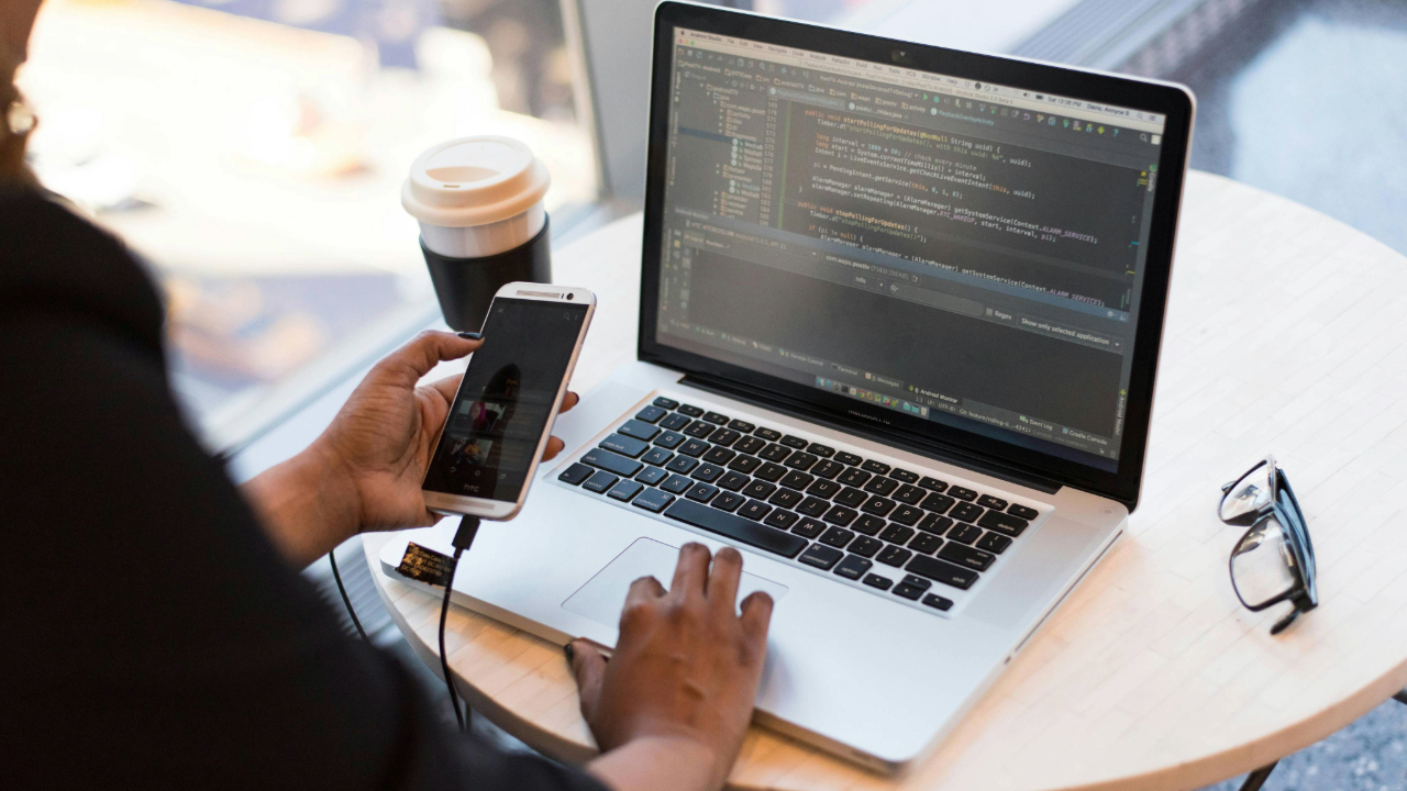 A stock photo showing someone transferring data from a mobile phone to a laptop.