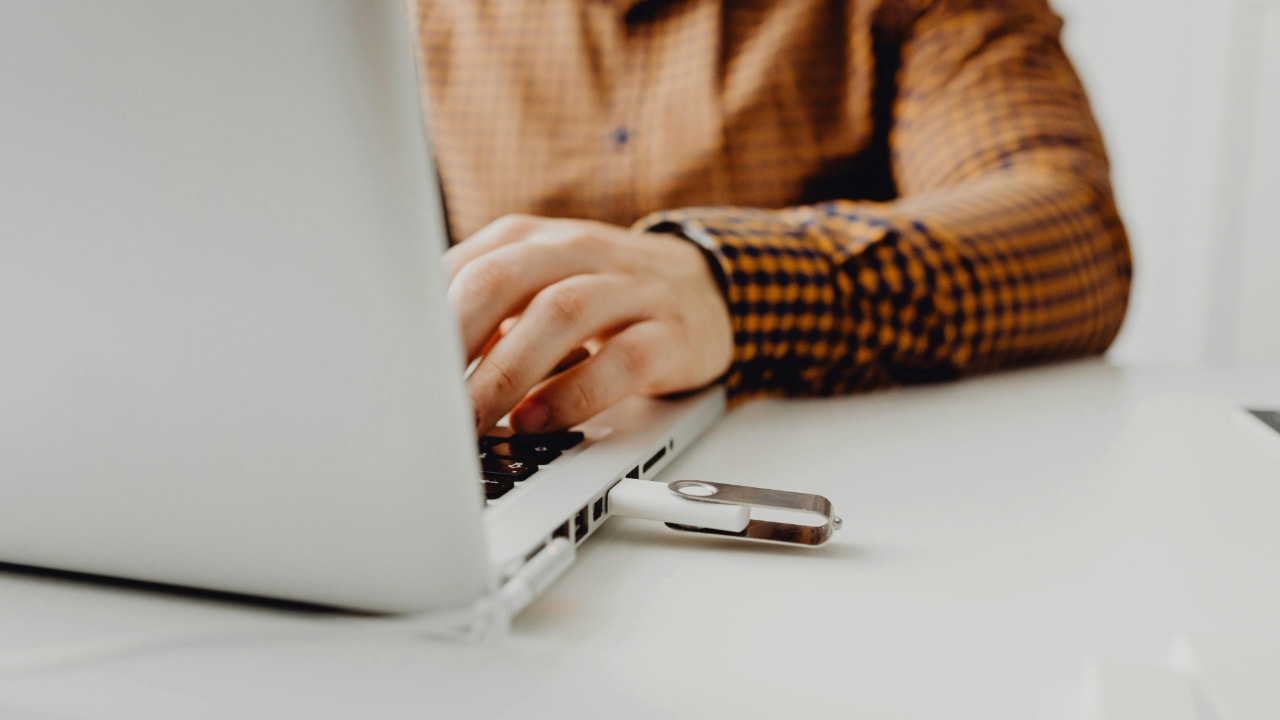 A person is working on a laptop with USB drive plugged in