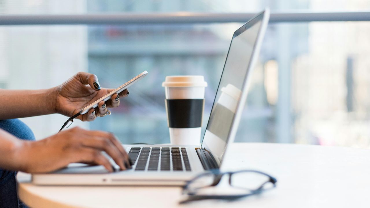 A woman working on her laptop and looking at her phone