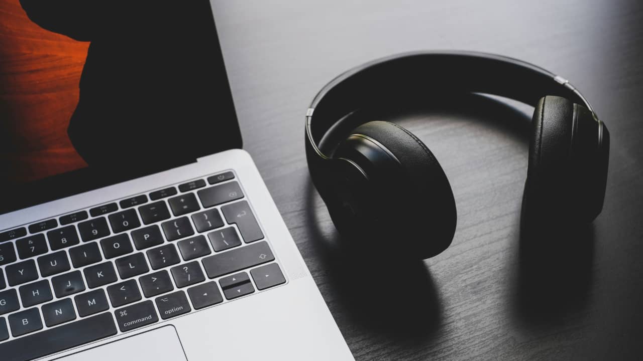 A pair of Bluetooth headphones next to a laptop