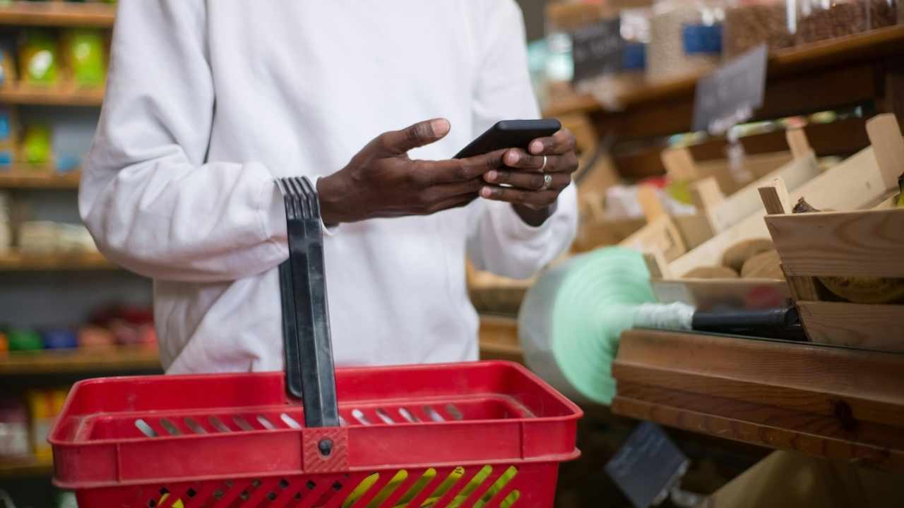 A shopper checks a phone in the grocery aisle, where the right app can help spot savings before checkout.
